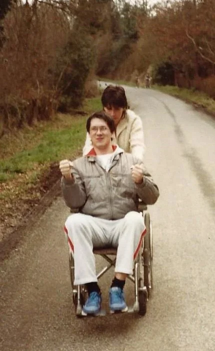 A woman pushing John Murphy in a wheelchair along a country lane